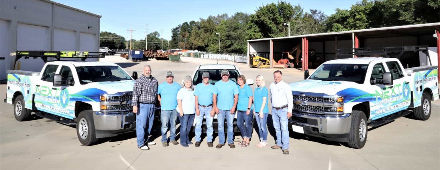 NEXT employee group photo in front of fleet of trucks.