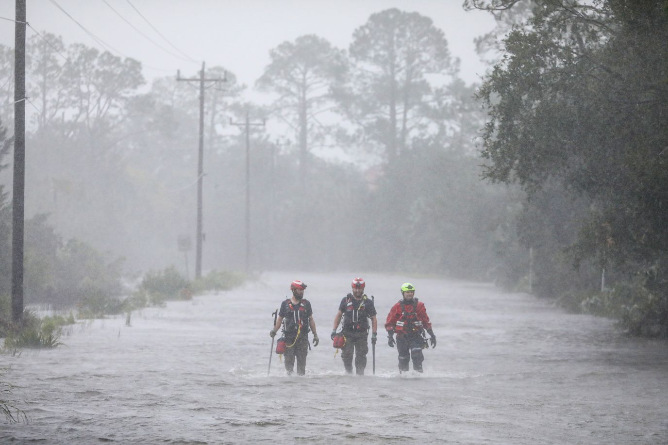 Three workers walk up a road that has been flooded with water.