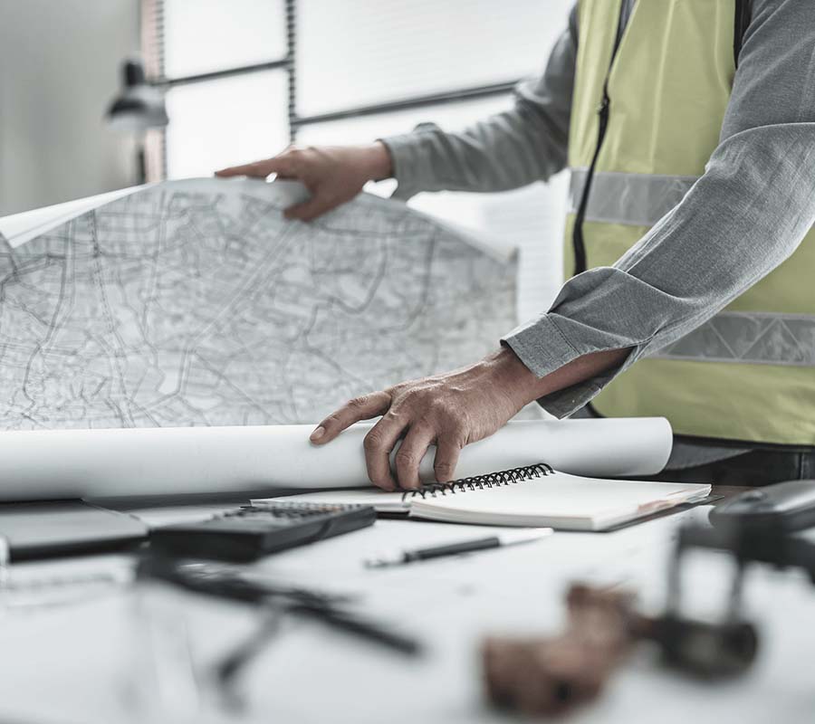 A man in a high-vis vest opens a large map on a workbench.