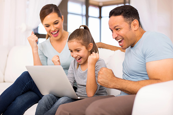 A family smiles and cheers while watching their laptop screen.