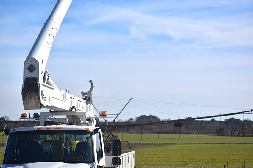 A boom truck with it's arm extended up in a field.