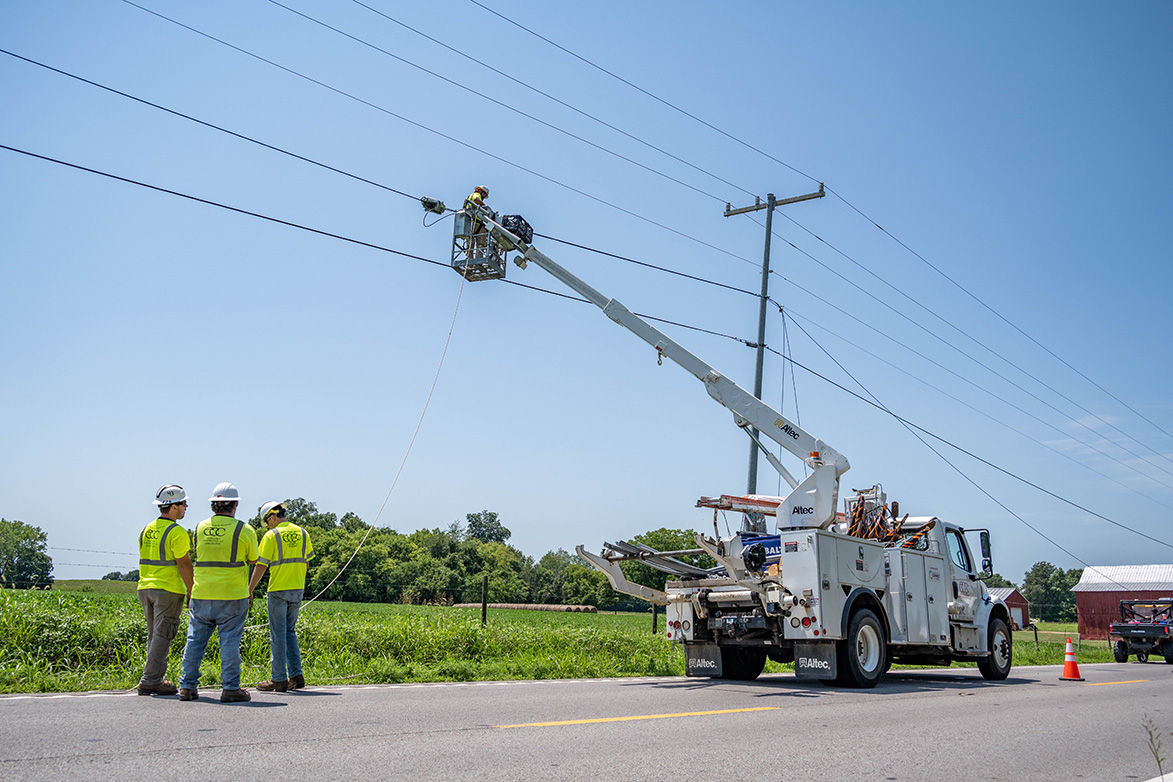 A cherry picker truck holds up an electrician to electrical wires along the road.