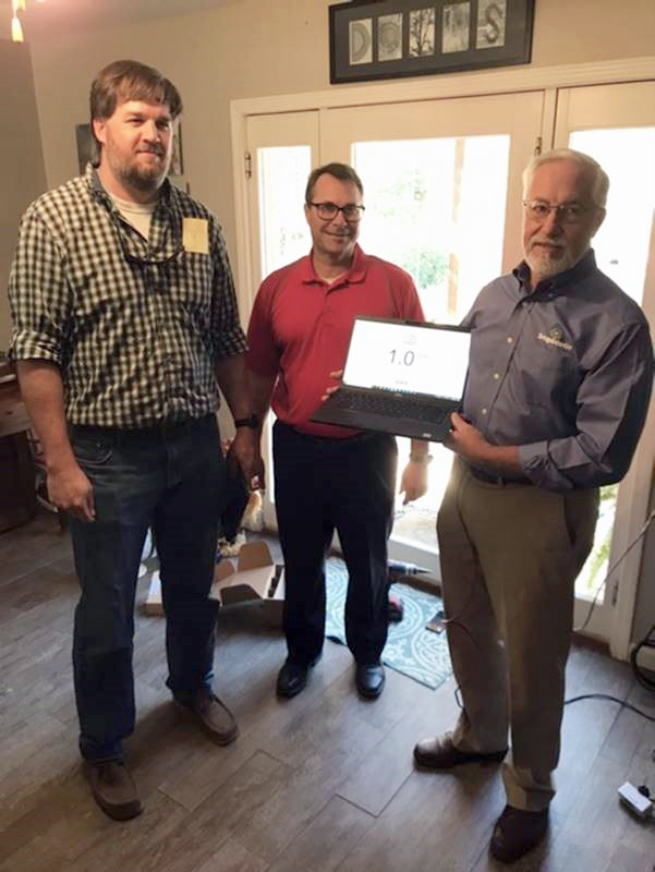 Three men stand and hold a computer showing a speed test.