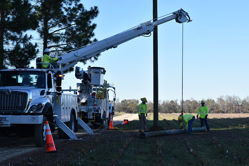 A crane truck lifting power poles for workers to put in the ground.
