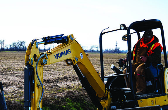 Construction worker operating a excavator in a field.
