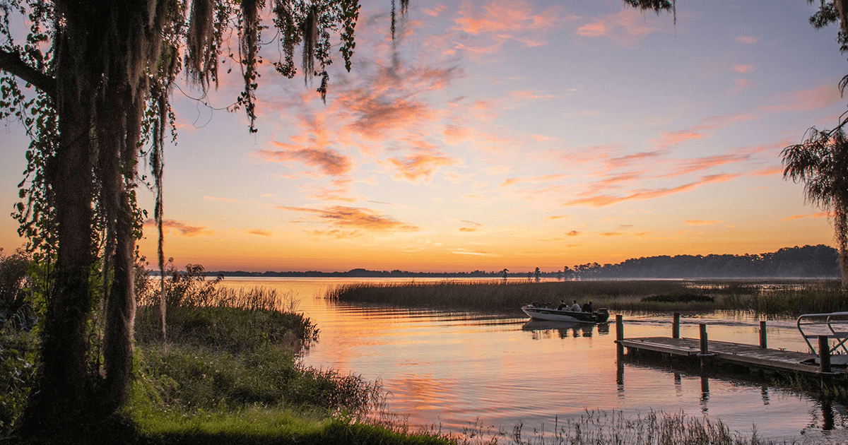 A dock perched over a lake with grassy marshes at sunset.