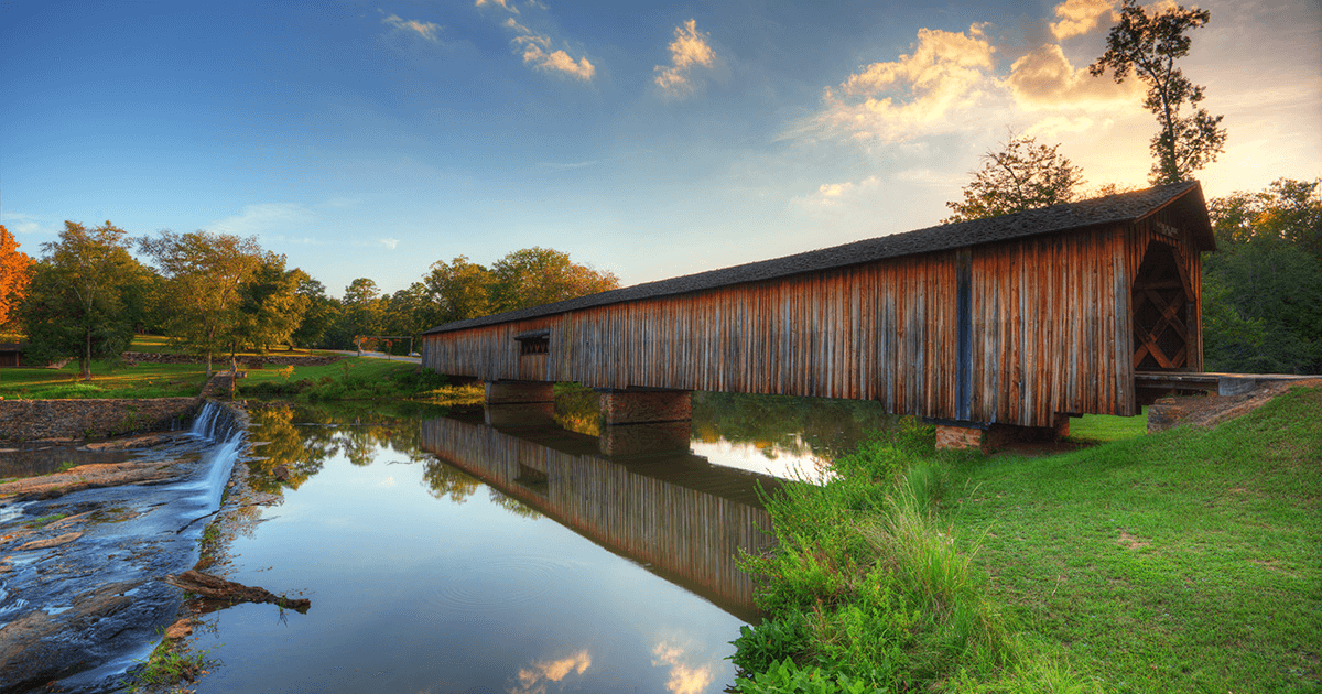 A covered bridge goes across a large river at sunrise.