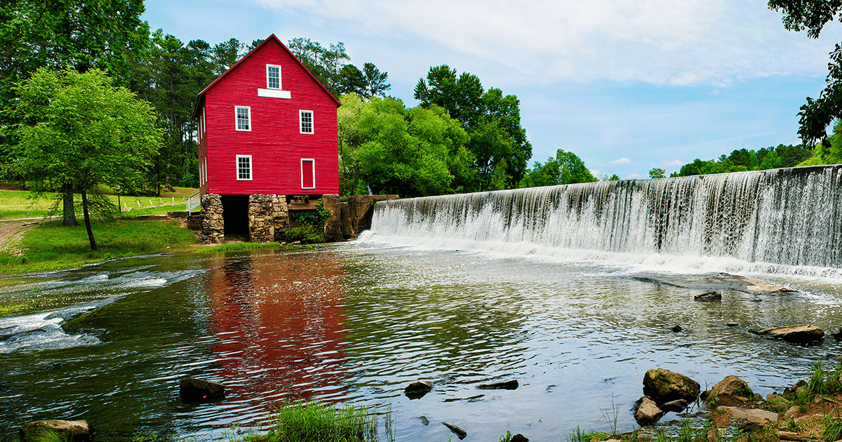 A large red barn with a water mill next to a man man waterfall and river.