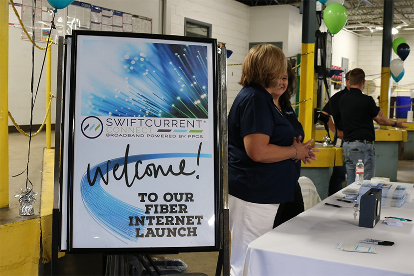 Ambassadors for Swift Current Connect stand behind a desk at a trades show.