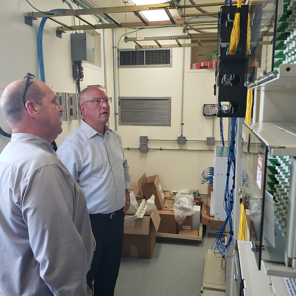 Two technicians stand in a network room looking at servers.