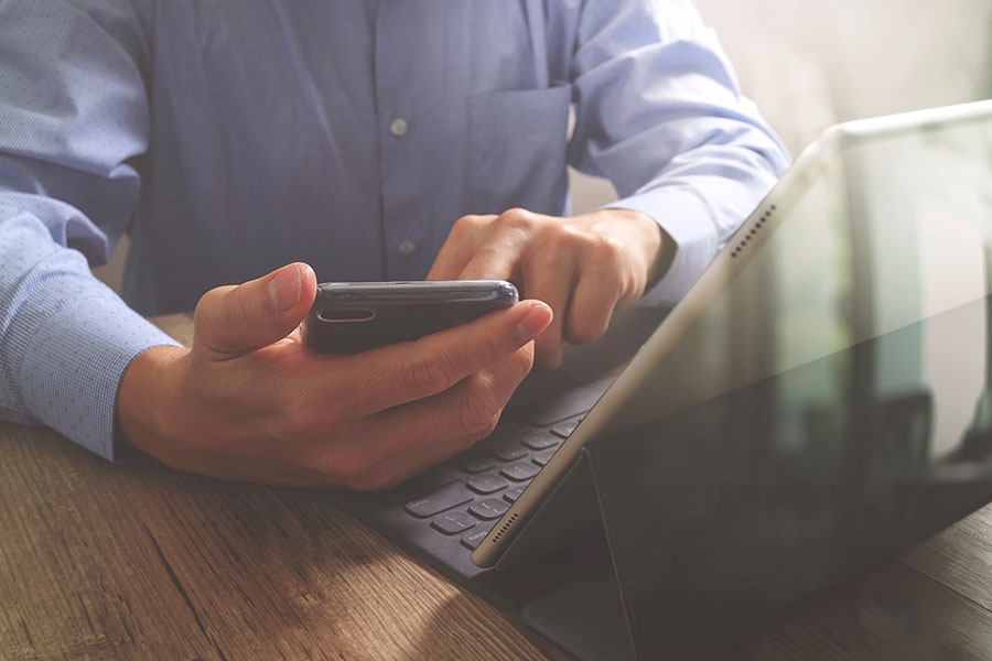 Man holding phone and using his computer at a desk.