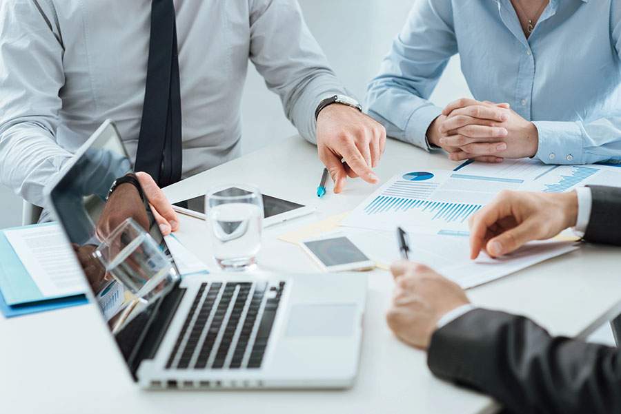 A group of office workers sits around a desk talking about paper and statistics.