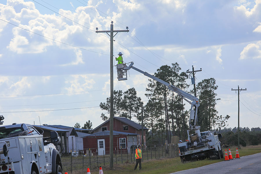 Technicians work on a power pole from a lift truck in a rural area.