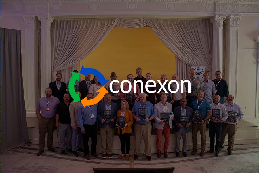 100 club inductees stand on stage holding their awards at co-ops connect 2025 with conexon logo and black matt overtop.